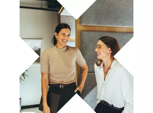 Dos mujeres sonrientes en una oficina moderna, representando un ambiente de trabajo colaborativo y positivo.