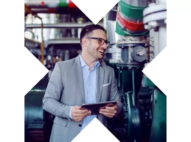 Hombre sonriente en una planta industrial, sosteniendo una tablet mientras trabaja.